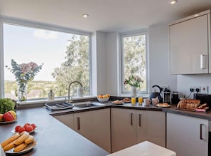 A modern kitchen with a large window, a sink, and a countertop with various items. - Cottage Sleeps 5 With Parking and Garden (Amlwch)