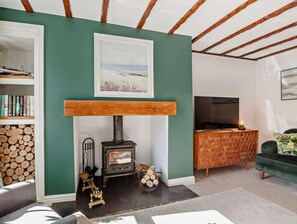 A cozy living room with a fireplace, bookshelves, a TV, and a green wall. - Cottage Sleeps 5 With Parking and Garden (Amlwch)