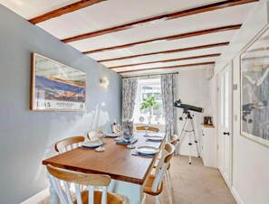 A dining area with a wooden table set for four, a telescope, and a framed picture on the wall. - Cottage Sleeps 5 With Parking and Garden (Amlwch)