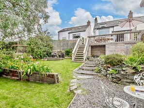 A garden with a wooden staircase leading to a house, a stone wall, and a table with a chair. - Cottage Sleeps 5 With Parking and Garden (Amlwch)