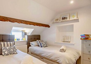 A bedroom with two beds, a window, a radiator, and a shelf with books. - Cottage Sleeps 5 With Parking and Garden (Amlwch)