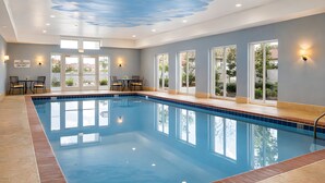 En indendørs swimmingpool med krystalklart, blåt vand, flisegulv og et loft med et sky-design.