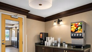 Et reception område med kaffemaskine, frugtanretning og en dør til en gang.
