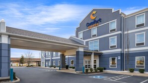 Et Comfort Suites hotel med overdækket indgang, parkeringsplads og en klar blå himmel.