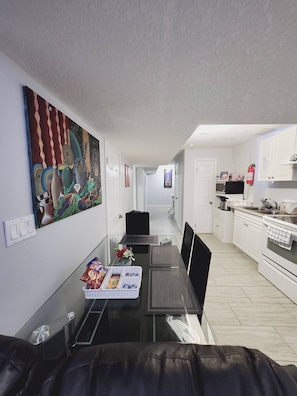 Una cocina moderna con armarios blancos, una estufa y un comedor con mesa y sillas de vidrio.
