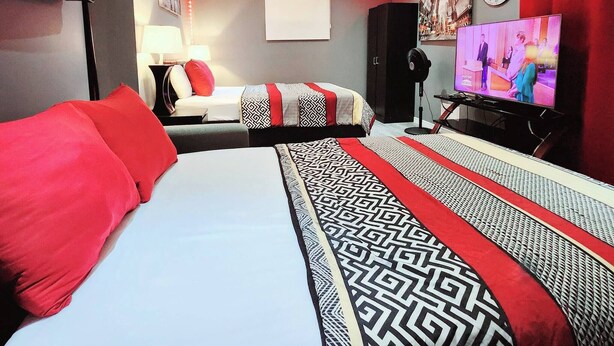A hotel room with a large bed, a TV, a desk, and a chair. - Staycation Studio Apartment (London)