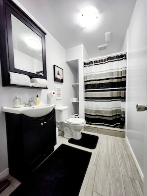 Baño con lavamanos, inodoro, espejo y cortina de ducha a rayas.
