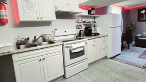 A kitchen with white cabinets, a stove, a sink, and a refrigerator. There are red LED lights along the ceiling edge. - Staycation Studio Apartment (London)