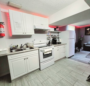 Una cocina con armarios blancos, estufa, fregadero y refrigerador. Hay luces LED rojas a lo largo del borde del techo.