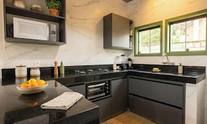 A modern kitchen with a marble countertop, built-in oven, microwave, and a window with green frames. - Refúgio Bichinho (Prados)