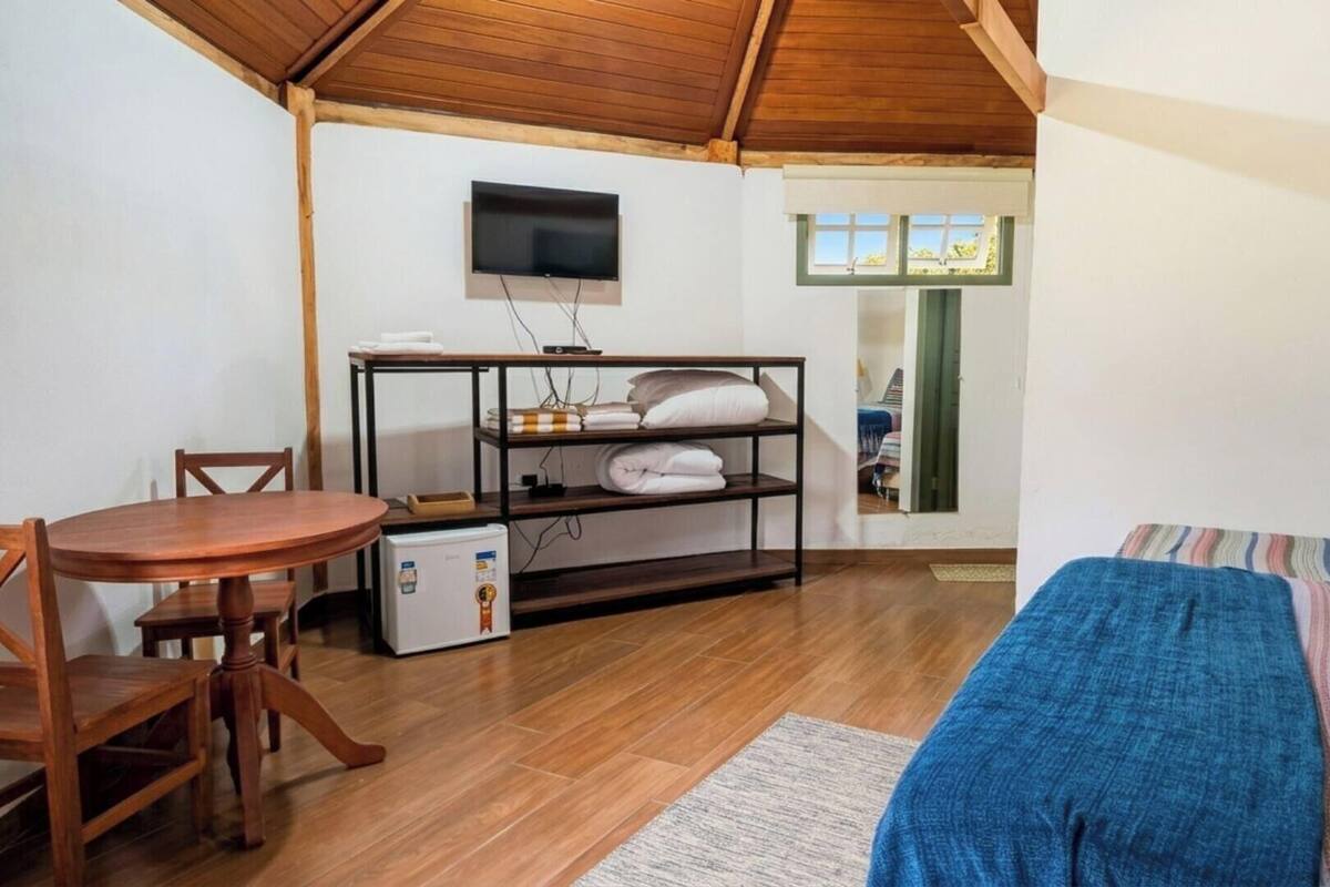 Une pièce chaleureuse avec un plafond en bois, un téléviseur fixé au mur, une petite table avec des chaises, un lit recouvert d’une couverture bleue et une étagère avec des serviettes pliées.