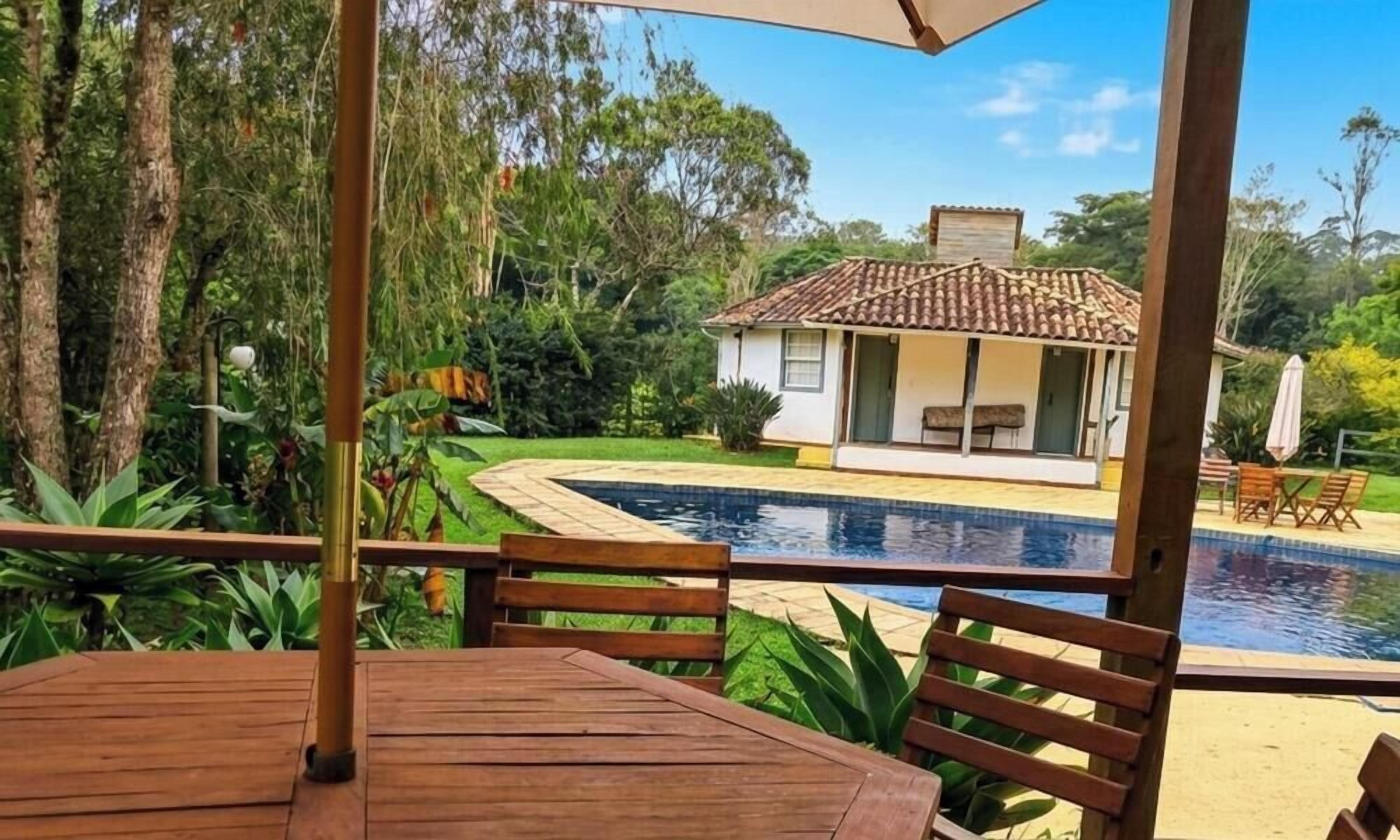 Une terrasse en bois avec une piscine, une petite maison avec un toit en tuiles et une végétation luxuriante.