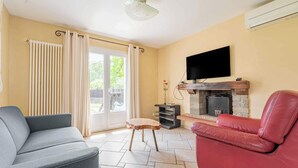 A living room with a grey sofa, a red leather chair, a fireplace, and a television mounted on the wall. - Air-conditioned house with pool, sleeps 6 (Carcassonne)