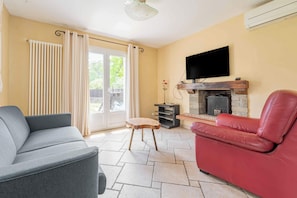 Ein Wohnzimmer mit grauem Sofa, einem roten Ledersessel, einem Kamin und einem an der Wand befestigten Fernseher.