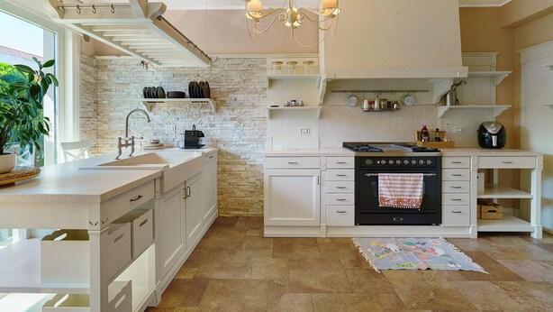 Una cocina moderna con armarios blancos, salpicadero de piedra y horno empotrado.