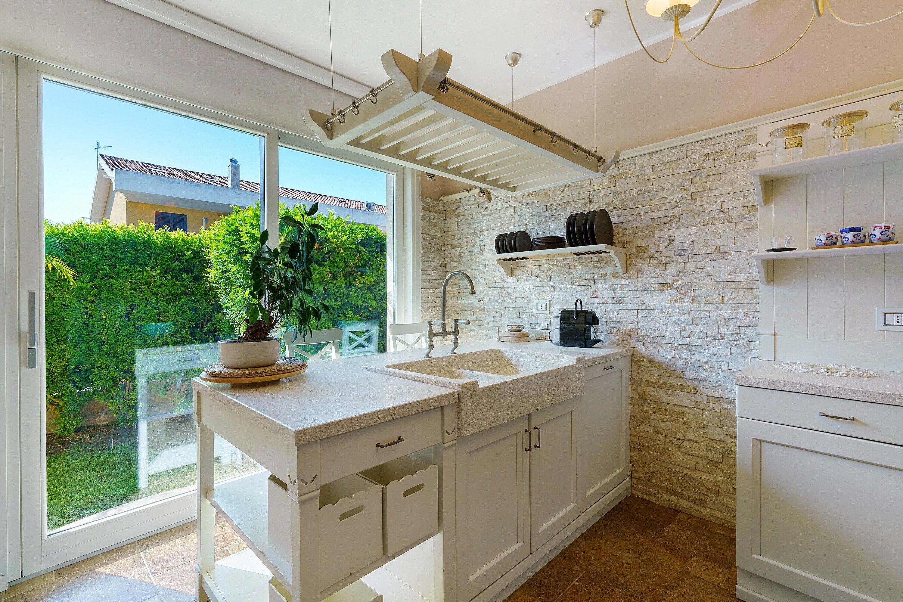 Una cocina moderna con una isla grande, armarios blancos, salpicadero de piedra y vista a un jardín a través de una puerta corrediza de vidrio.