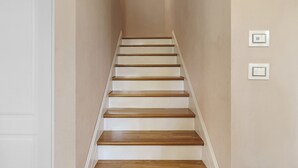 Una escalera con escalones de madera y paredes blancas, que lleva a una puerta al final.