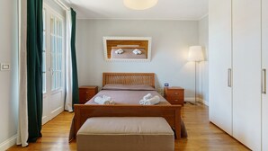 Un dormitorio con una cama de madera, una mesita de noche, una lámpara, un espejo y una ventana con cortinas.
