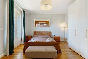Ein Schlafzimmer mit einem hölzernen Bett, einem Nachttisch, einer Lampe, einem Spiegel und einem Fenster mit Vorhängen.