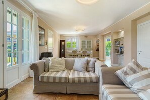 Ein geräumiges Wohnzimmer mit einer großen Couch, einem Essbereich und einer durch eine offene Tür einsehbarer Küche.