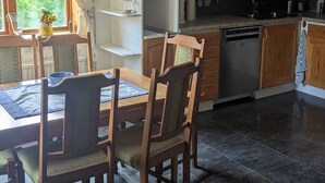 Keittiössä on tummat laatat, puiset kaapit, ruokapöytä tuoleineen ja ikkuna, jossa on verhot.