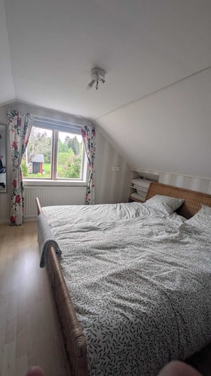 Un dormitorio con techo inclinado, una cama con ropa de cama estampada, un radiador y una ventana con cortinas.