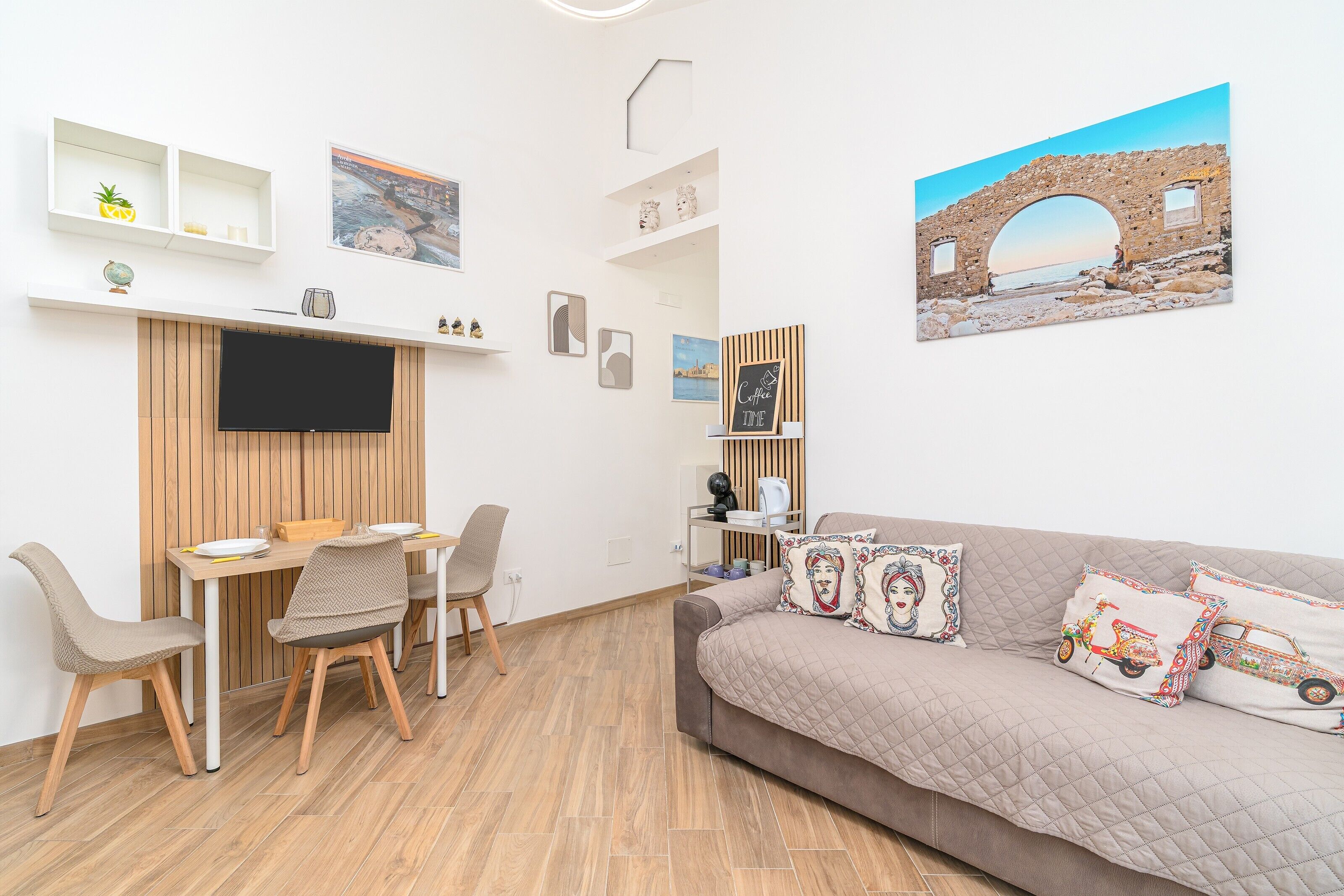 Ein modernes Wohnzimmer mit Fernseher, Esstisch, Stühlen, einer Couch und einem Wandregal mit Dekoration.