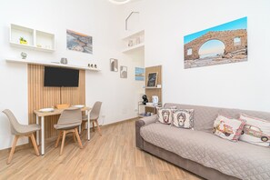 Ein modernes Wohnzimmer mit Fernseher, Esstisch, Stühlen, einer Couch und einem Wandregal mit Dekoration.