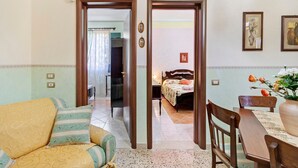 Una habitación con cama, sofá, mesa de comedor y una silla. Hay dos puertas que dan a otra habitación.