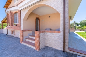 A building with a curved facade, brick steps leading to an entrance, and a covered outdoor seating area. - Apartment 'Magnolia' with Pool, Wi-Fi and Air Conditioning (Arenella)