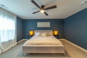 Un dormitorio con una cama, dos lámparas de noche, un ventilador de techo y una ventana con cortinas.