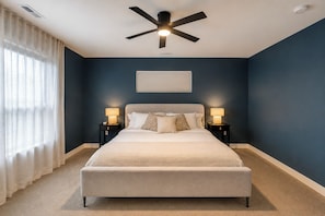 A bedroom with a bed, two bedside tables with lamps, a ceiling fan, and a window with curtains. - Brand-New 2026 Home • Near Downtown (Indianapolis)