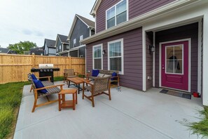 Un patio con mobiliario exterior, una parrilla y una valla de madera.