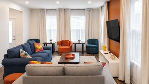 Ein modernes Wohnzimmer mit einer Couch, Sesseln, einem Couchtisch und einem Fernseher.