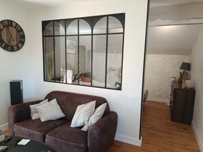 A room with a brown leather sofa, a large window with a view, a clock, and a desk with a lamp. - "Gîte des Cerisiers" Apartment with Pool, Terrace and Private Garden (Saint-Germain-de-Belvès)