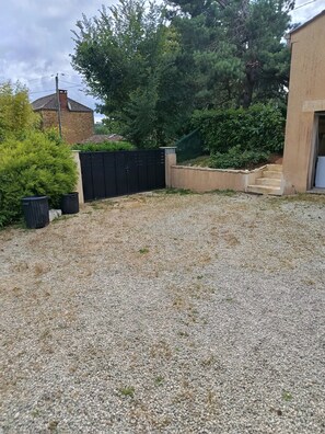 A gravel driveway leading to a house with a black fence, a tree, and a small garden area. - "Gîte des Cerisiers" Apartment with Pool, Terrace and Private Garden (Saint-Germain-de-Belvès)
