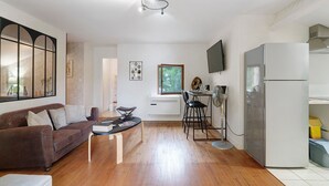 A modern living room with a brown sofa, a dining table, and a kitchen area with a refrigerator and a TV.