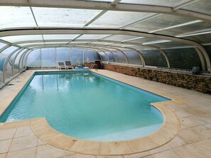Une piscine intĂ©rieure au design incurvĂ©, entourĂ©e dâun mur de pierre et protĂ©gĂ©e par une paroi en verre.