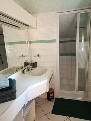 Une salle de bain avec un lavabo blanc, un miroir et un espace douche.