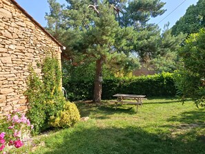 Un bĂątiment en pierre avec une cour verdoyante, un arbre et une table de pique-nique.