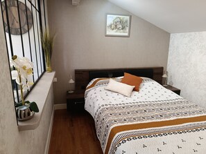 Une chambre Ă coucher avec un lit, une table de chevet, une horloge murale, un tableau encadrĂ© et une fenĂȘtre avec des plantes.