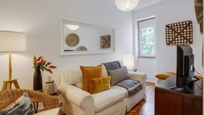 A living room with a sofa, a TV, a lamp, and a window with a view. - Spacious Tailor Made Flat in Areeiro (Lisbon)