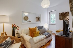A living room with a sofa, a TV, a lamp, and a window with a view. - Spacious Tailor Made Flat in Areeiro (Lisbon)