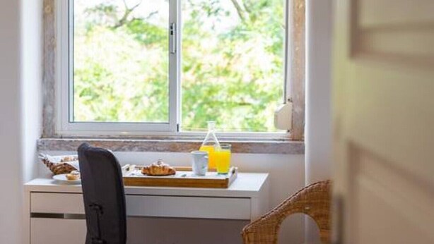A hotel room with a bed, a desk with breakfast items, a chair, and a window with a view of greenery. - Spacious Tailor Made Flat in Areeiro (Lisbon)