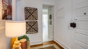 A hallway with white walls, a wooden floor, a lamp, and two wall-mounted decorative items. - Spacious Tailor Made Flat in Areeiro (Lisbon)