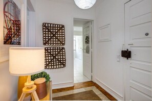 A hallway with white walls, a wooden floor, a lamp, and two wall-mounted decorative items. - Spacious Tailor Made Flat in Areeiro (Lisbon)