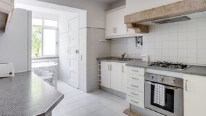 A kitchen with white cabinets, a gas stove, an oven, and a window providing natural light. - Spacious Tailor Made Flat in Areeiro (Lisbon)