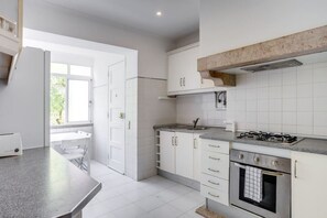 A kitchen with white cabinets, a gas stove, an oven, and a window providing natural light. - Spacious Tailor Made Flat in Areeiro (Lisbon)