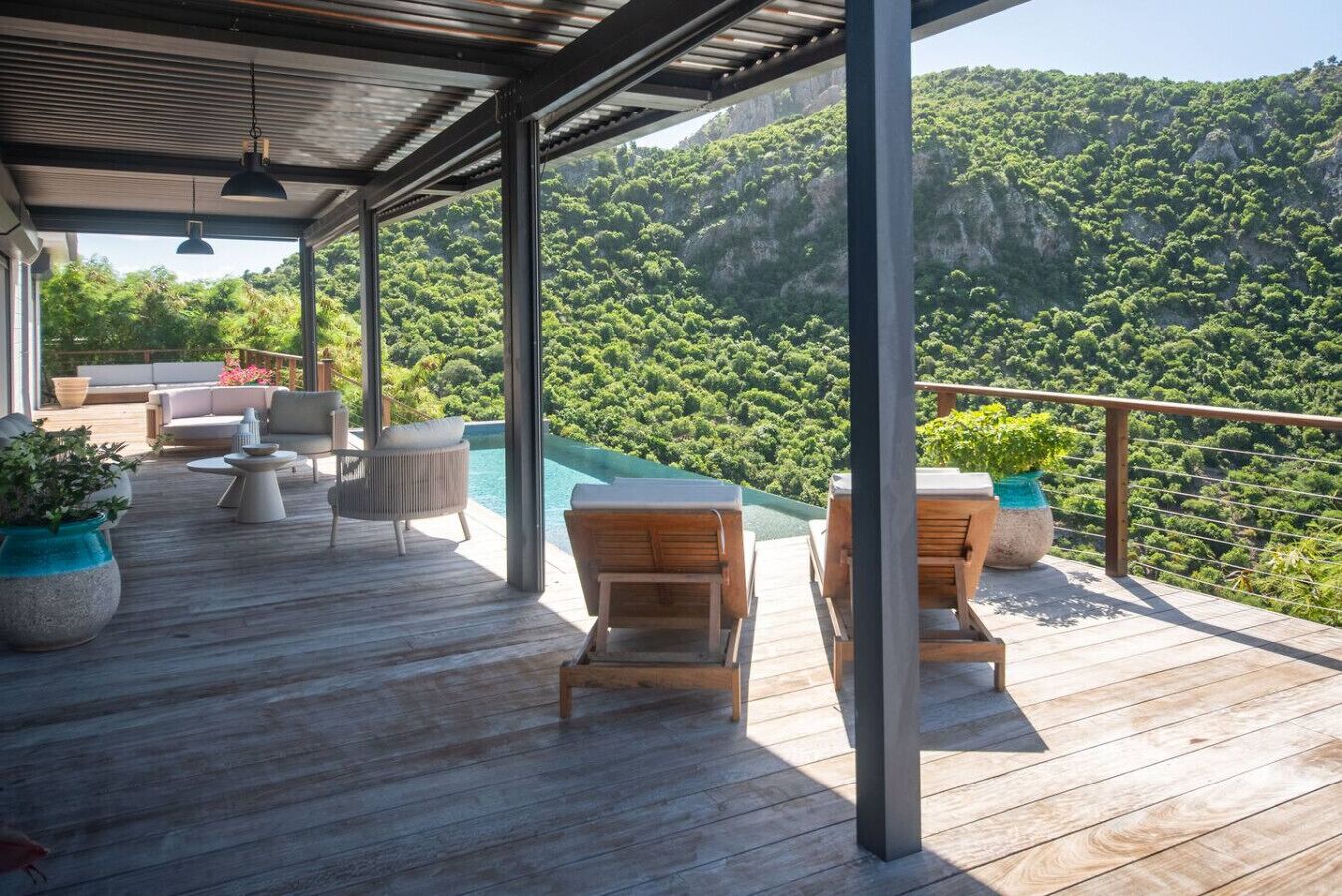 A wooden deck with outdoor furniture, a pool, and a mountainous backdrop.