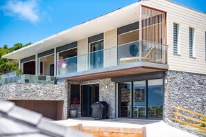 Ein modernes, zweistöckiges Haus mit Natursteinfassade, einem Balkon mit Glasgeländern und einem Whirlpool im Vorgarten.